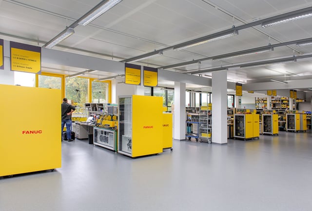 Werkstatt mit Arbeitstischen und gelben Schaltschränken mit der Aufschrift „Fanuc“