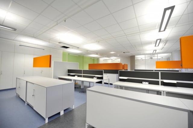 Bürofläche mit weißen Schränken, Schreibtischen und orangen Trennwänden vor einer grünen Wand