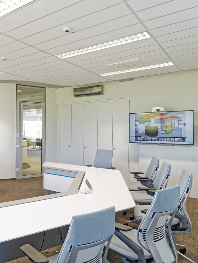 Besprechungsraum mit geschwungenem weißem Tisch, hellblauen Bürostühlen und Bildschirm an der Wand