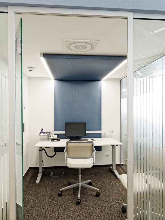 Kleiner Einzelarbeitsraum hinter Glas mit Schreibtisch, Bildschirm und blau bespannter Wand