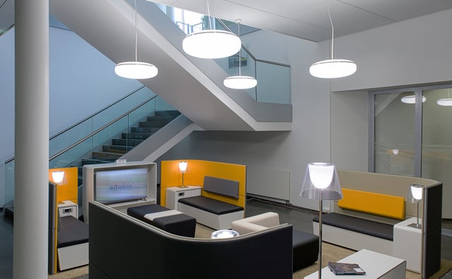 Lounge mit Sitzbänken, Bildschirm und Leuchten unter einer Treppe