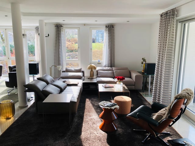 Wohnzimmer mit Ecksofa, Couchtisch und Lounge-Sessel auf dunklem Teppich
