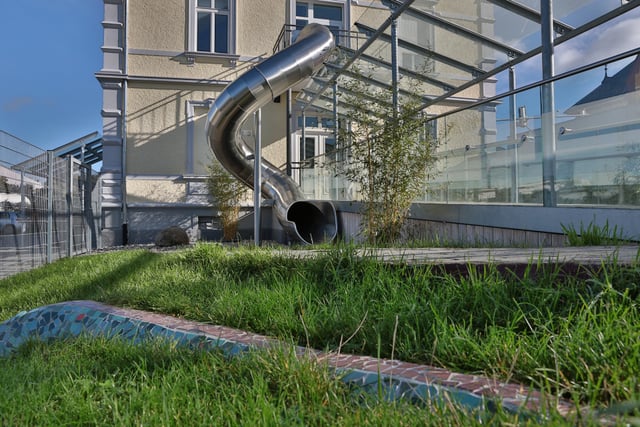 Rutsche aus Edelstahl an einer Terrasse mit Glasgeländer, davor Rasen
