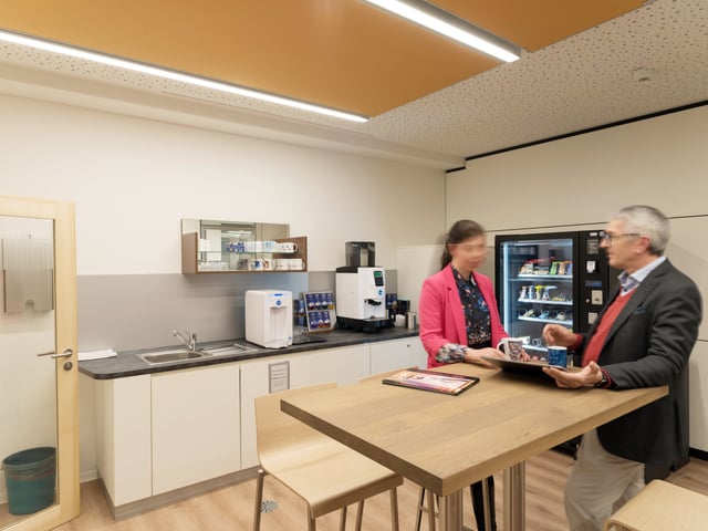 Zwei Personen im Gespräch an einem Stehtisch aus Holz in einer Teeküche