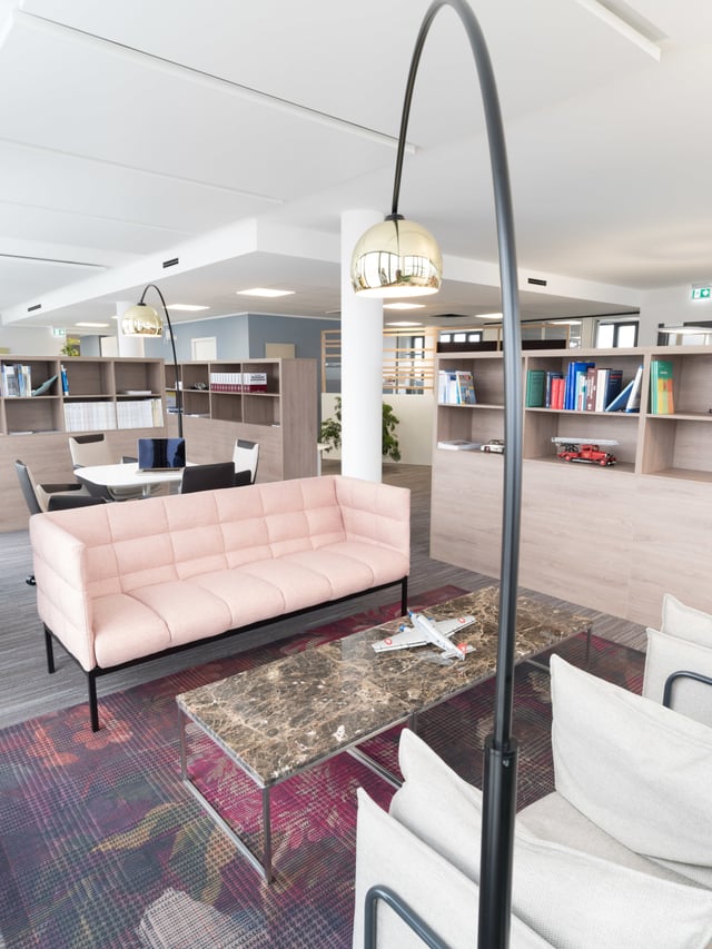 Wartebereich mit rosa Sofa, Marmortisch, weißen Sesseln und Bogenleuchte vor Bücherregalen