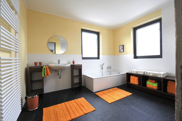 Badezimmer mit gelben Wänden, Badewanne, Waschbecken und orangen Badvorlegern