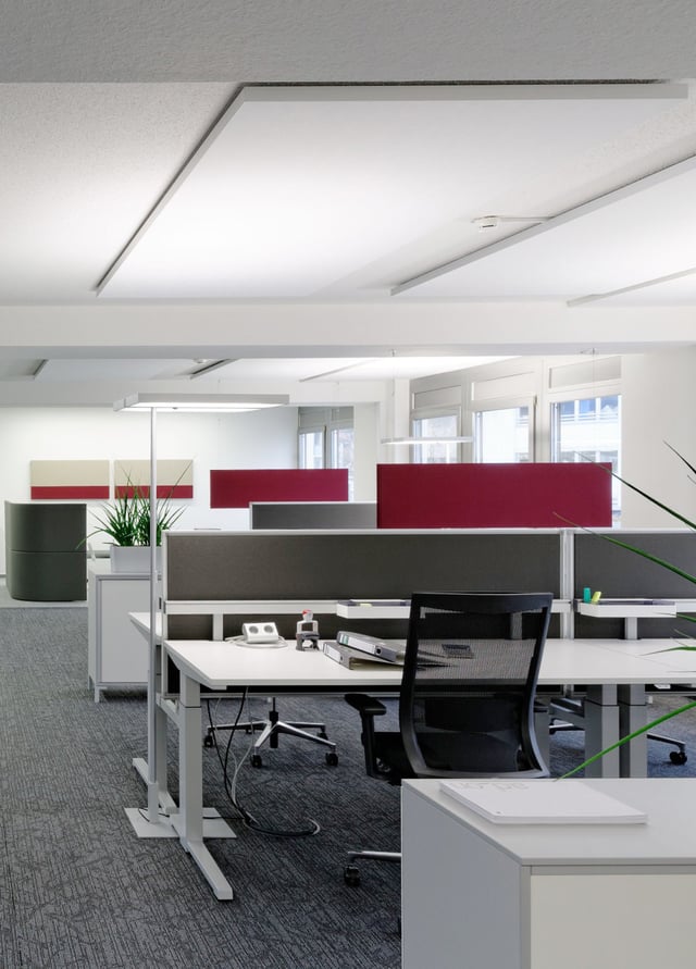 Schreibtisch mit Bürostuhl und Trennwänden in Grau und Rot unter Akustiksegeln