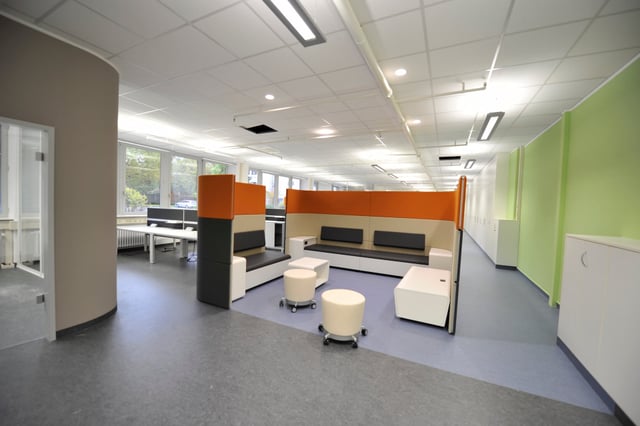 Lounge mit orangen Trennwänden, Sitzbänken, Hockern und Sitzwürfeln in einer Bürofläche