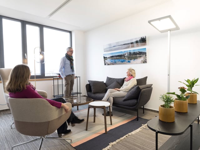 Lounge mit Sesseln und dunklem Sofa, drei Personen im Gespräch