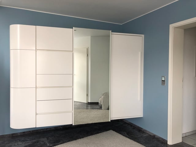Weißer Wandschrank mit Spiegeltür vor einer hellblauen Wand