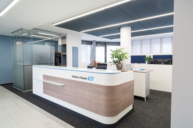 Empfangstheke in Weiß und Holzoptik mit dem Schriftzug Endress+Hauser, dahinter Arbeitsplätze