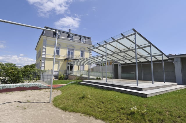 Gelbe Villa mit Terrasse unter einem Glasdach und Rasenfläche