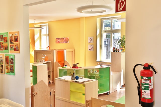 Kita-Raum mit Holzmöbeln in Grün und Gelb und Kinderbildern an der Wand