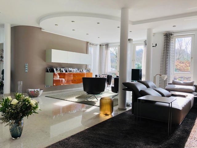 Wohnzimmer mit hellem Steinboden, Ledersofa, Sesseln und orangem Sideboard