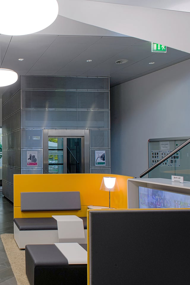 Sitzbank mit gelber Rückwand und Leselampe vor einem Aufzug