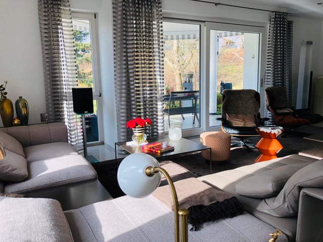 Wohnzimmer mit Sofas, Couchtisch mit roten Blumen und Lounge-Sesseln am Fenster
