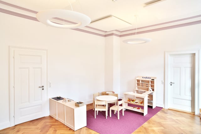 Spielzimmer mit Kinderkaufladen, kleinem Tisch und Stühlen auf lila Teppich