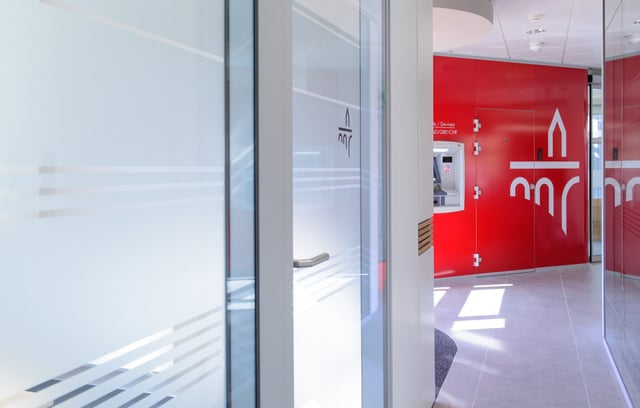 Glastüren mit Streifenfolie, dahinter rote Wand mit Logo und Geldautomat